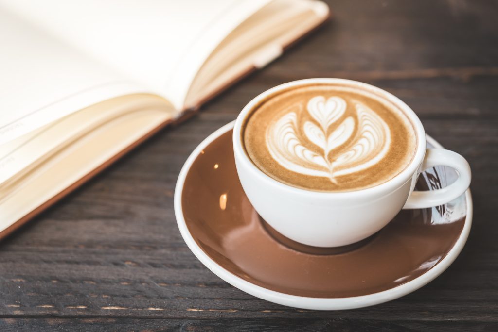 Tasse de café latte façon latte art sur table en bois avec livre ouvert