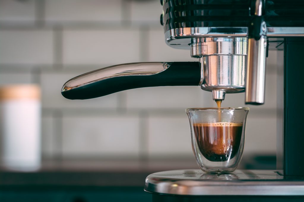 premier plan d'une machine à café professionnelle avec un espresso qui coule dans une tasse transparente